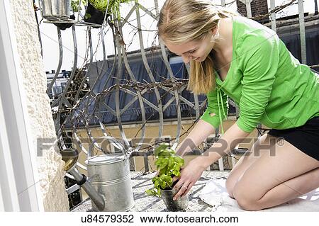 Stock Image - Teenage girl on balcony with pot plant. Fotosearch