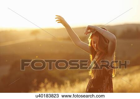 Stock Image - Teenager dancing in field at dusk. Fotosearch
