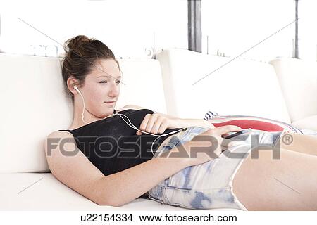 Teenager lying on bed listening to music View Large Photo Image Picture - Teenager lying on bed listening to music. Fotosearch