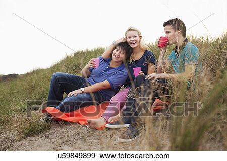 Stock Photo - Teenagers sitting on bin bag, having drink. Fotosearch