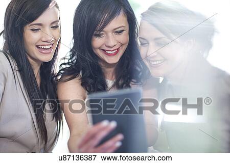 Stock Photo - Three female friends looking at digital tablet. Fotosearch