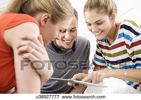 Three young adult friends using digital tablet View Large Photo Image Stock Photo - Three young adult friends using digital tablet. Fotosearch
