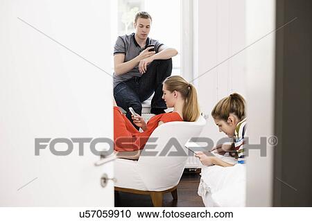 Three young adult friends using mobiles and digital tablet in bedroom View Large Photo Image Stock Image - Three young adult friends using mobiles and digital tablet in bedroom. Fotosearch