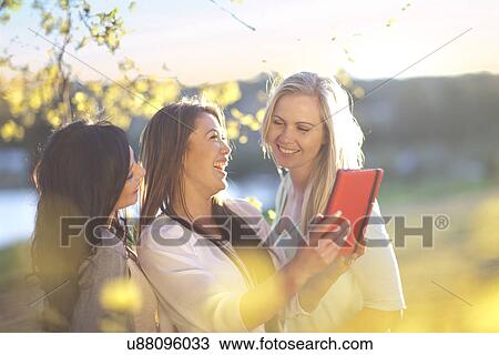 Three young women looking at digital tablet in park View Large Photo Image Stock Image - Three young women looking at digital tablet in park. Fotosearch