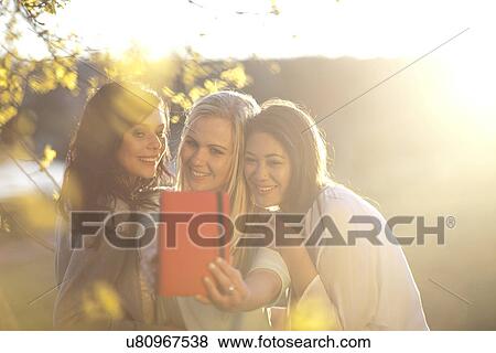 Stock Photo - Three young women taking self portrait in park. Fotosearch