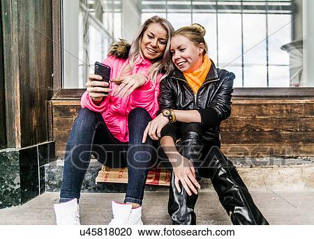 Two female friends looking at mobile phone View Large Photo Image Stock Image - Two female friends looking at mobile phone. Fotosearch