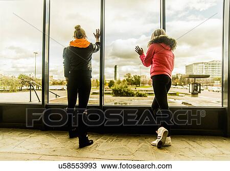 Two female friends looking out of window View Large Photo Image Stock Image - Two female friends looking out of window. Fotosearch