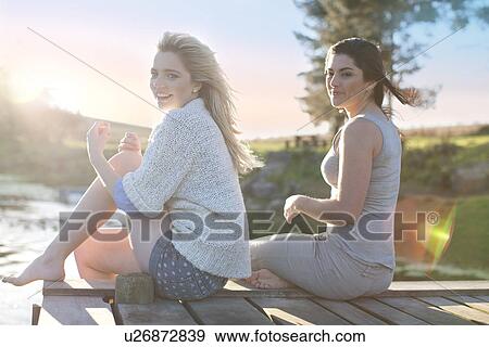 Two female friends sitting on breezy pier View Large Photo Image Stock Photo - Two female friends sitting on breezy pier. Fotosearch