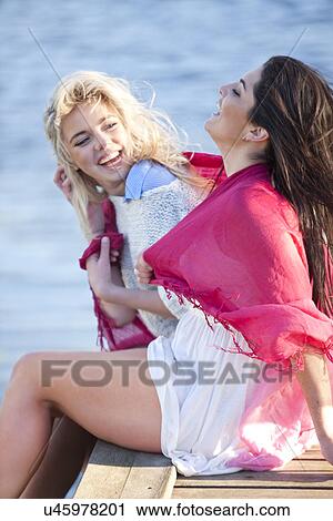 Two female friends sitting on pier laughing View Large Photo Image Stock Image - Two female friends sitting on pier laughing. Fotosearch