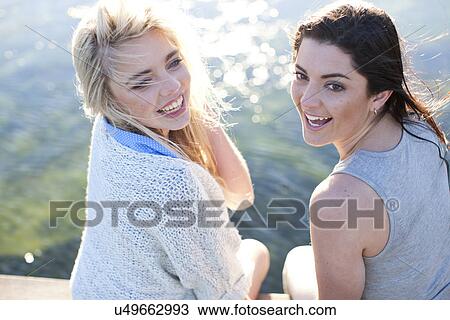 Stock Image - Two female friends sitting on pier. Fotosearch