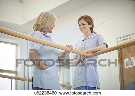 Stock Image - Two female nurses chatting on hospital atrium balcony. Fotosearch