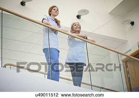 Stock Image - Two female nurses waiting on hospital atrium balcony. Fotosearch