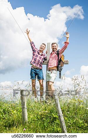 Stock Image - Two male friends by cross with arms up. Fotosearch