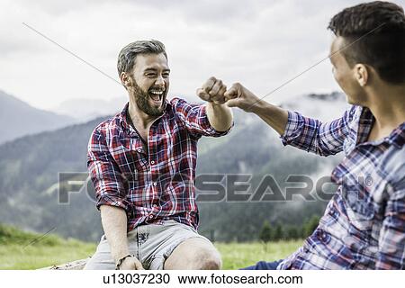 Stock Image - Two male friends sitting on fence, Tyrol Austria. Fotosearch