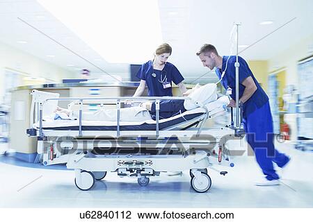 Stock Image - Two medics pushing gurney in hospital emergency room. Fotosearch
