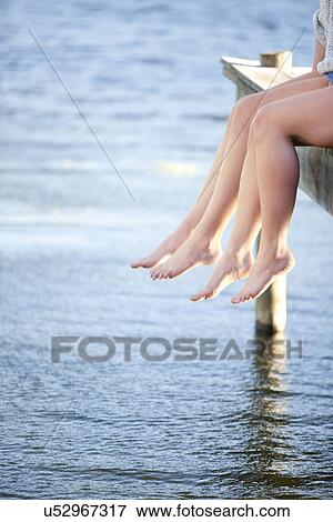 Stock Photo - Two pairs of female legs dangling from pier. Fotosearch