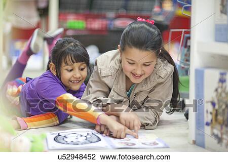 Stock Image - Two sisters looking at picture book in toy shop. Fotosearch