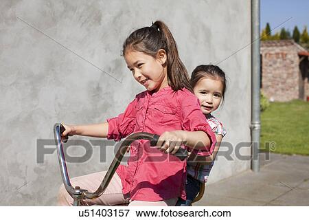 Two sisters playing on tricycle View Large Photo Image Stock Photo - Two sisters playing on tricycle. Fotosearch