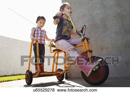 Two sisters playing on tricycle View Large Photo Image Stock Photo - Two sisters playing on tricycle. Fotosearch