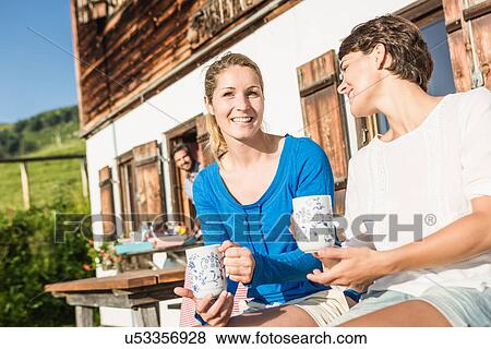 Stock Photo - Two women drinking coffee outside chalet, Tyrol, Austria. Fotosearch