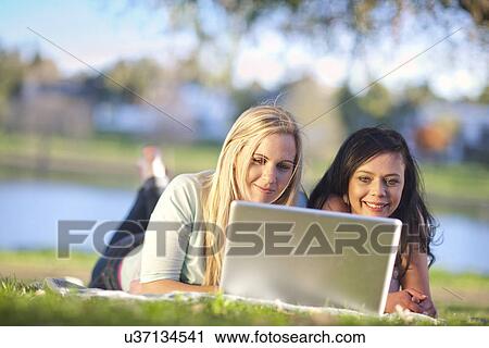 Stock Image - Two young women in park looking at laptop. Fotosearch