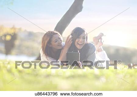 Two young women in park with digital tablet and earphones View Large Photo Image Stock Photograph - Two young women in park with digital tablet and earphones. Fotosearch