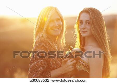 Woman and teenager standing in field at dusk holding domestic dog View Large Photo Image Stock Image - Woman and teenager standing in field at dusk holding domestic dog. Fotosearch