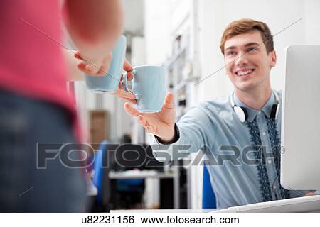 Woman giving young man coffee in office View Large Photo Image Stock Photograph - Woman giving young man coffee in office. Fotosearch