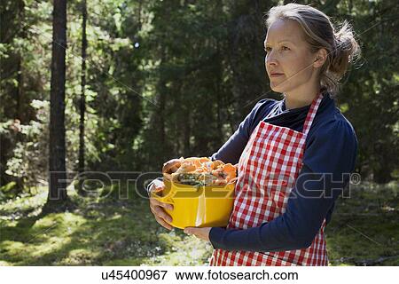 Stock Photo - Woman in forest with mushrooms in saucepan. Fotosearch