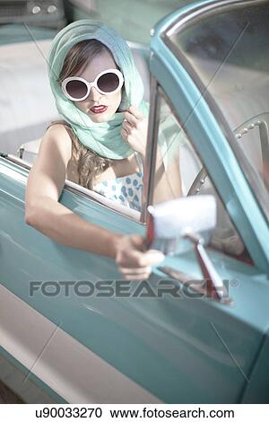 Stock Image - Woman in headscarf and white sunglasses in vintage convertible. Fotosearch