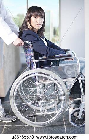 Stock Image - Woman in wheelchair assisted by male nurse. Fotosearch
