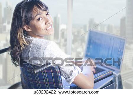 Stock Image - Woman in wheelchair turning around from laptop. Fotosearch