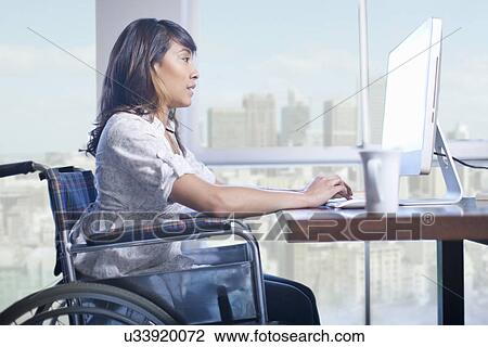 Stock Image - Woman in wheelchair using computer. Fotosearch