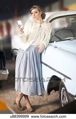 Stock Photo - Woman leaning on convertible texting. Fotosearch