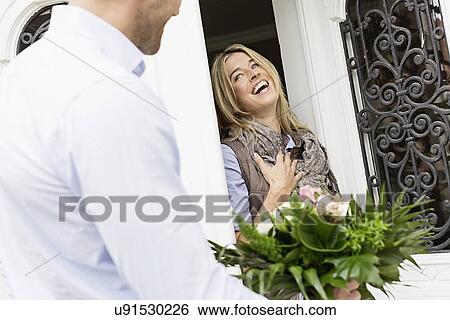 Stock Photograph - Woman opening front foor, man with bouquet. Fotosearch