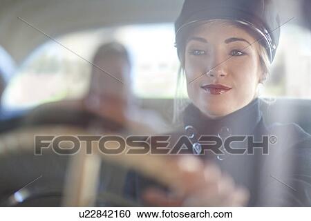 Stock Image - Woman playing chauffeur in vintage car. Fotosearch