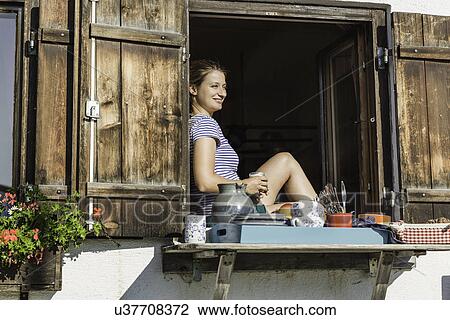 Stock Image - Woman sitting inside chalet window, Tyrol, Austria. Fotosearch