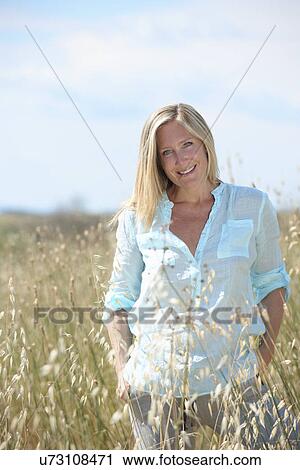 Stock Image - Woman standing in field with hands in pockets. Fotosearch