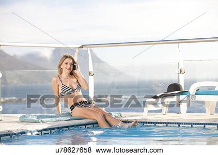 Stock Photo - Woman using cellular phone by swimming pool, Cape Town, South Africa. Fotosearch