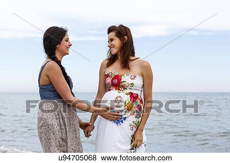 Stock Photo - Woman with hand on pregnant friend's stomach. Fotosearch
