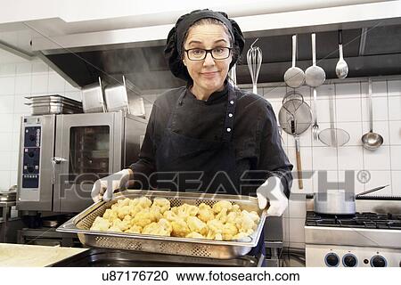 Stock Image - Woman working in restaurant kitchen, holding tray of cauliflower. Fotosearch