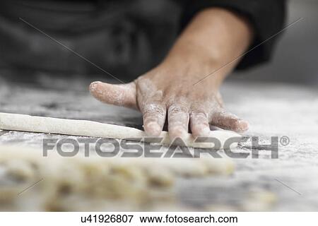 Stock Photo - Woman working in restaurant kitchen, cropped hand rolling pastry. Fotosearch