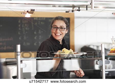 Stock Photo - Woman working in restaurant kitchen, serving meal. Fotosearch