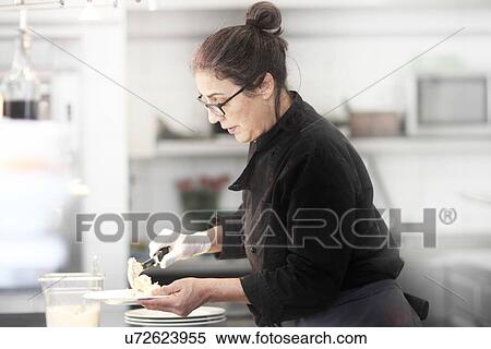 Stock Photography - Woman working in restaurant kitchen, serving meal. Fotosearch