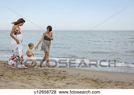 Stock Photo - Women and toddler walking along shore. Fotosearch