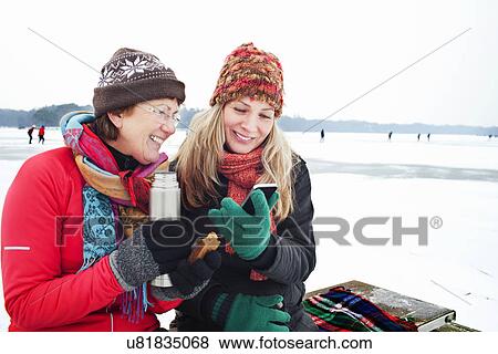 Stock Photo - Women having hot drinking and looking at smartphone. Fotosearch
