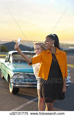 Women self-photographing in front of vintage car View Large Photo Image Stock Photography - Women self-photographing in front of vintage car. Fotosearch