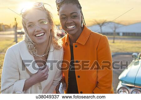 Stock Photo - Women smiling for camera in front of vintage car. Fotosearch