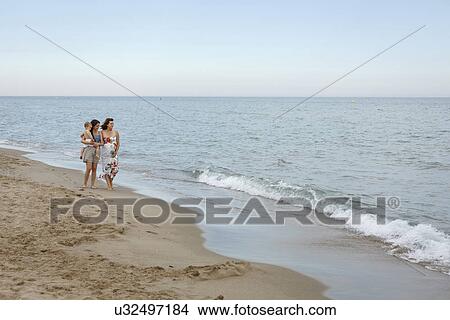 Women walking along shore with arm around, one pregnant, carrying toddler View Large Photo Image Picture - Women walking along shore with arm around, one pregnant, carrying toddler. Fotosearch