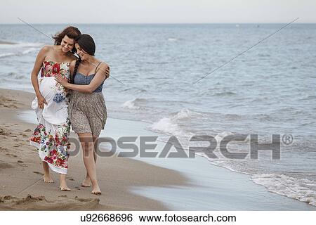 Women walking along shore with arm around, one pregnant View Large Photo Image Stock Photograph - Women walking along shore with arm around, one pregnant. Fotosearch
